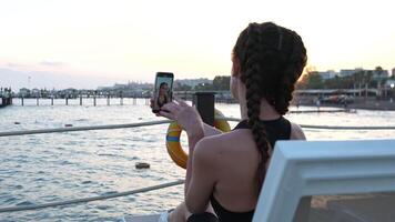 A girl lies on a sun lounger on a pier and takes a selfie video