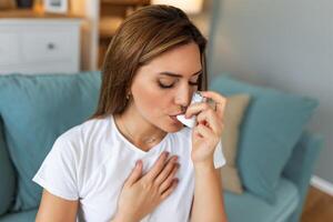 Woman using inhaler while suffering from asthma at home. Young woman using asthma inhaler. Close-up of a young woman using asthma inhaler at home. photo
