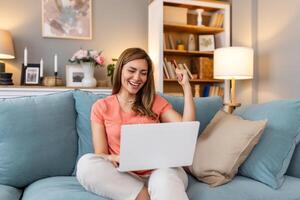 Young woman using laptop at home, looking at screen, chatting, reading or writing email, sitting on couch, female student doing homework, working on research project online photo