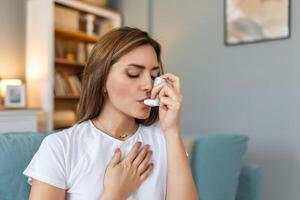 Woman using inhaler while suffering from asthma at home. Young woman using asthma inhaler. Close-up of a young woman using asthma inhaler at home. photo