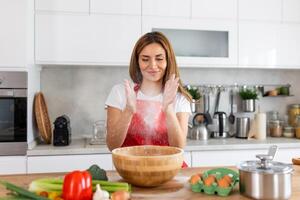 Young woman in apron prepares dough for baking in light kitchen interior. Got idea, cooking pizza, pie at home and facial expression, blowing flour photo