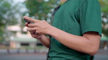 Close-up of a man with a backpack using a smartphone while walking on campus near the university building. A man is talking online with a friend using a social network. video