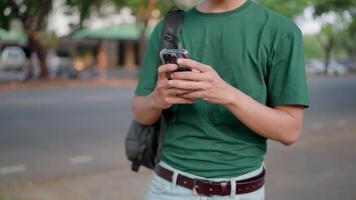 A man with a backpack uses a smartphone while walking in the university area near the university building. Man chatting online with friends Surf social networks video