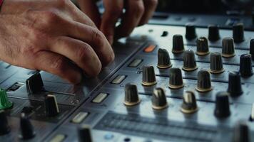 DJ carefully adjusting the settings of the mixer console during the live set. Musician is moving the faders with the hands on the controller close up video