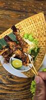 Chicken grilled satay skewers served with lime and peanut sauce on black, top view. Asian thai style food. photo