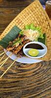 Chicken grilled satay skewers served with lime and peanut sauce on black, top view. Asian thai style food. photo