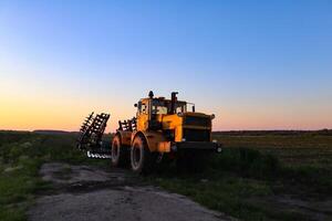 Cultivator on agricultural field at golden hour. Machine in field at sunset. photo