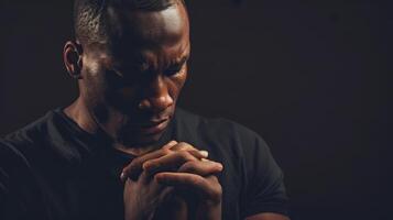Black man praying with folded hands isolated on a black background. photo