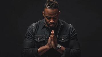Black man praying with folded hands isolated on a black background. photo
