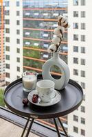 Coffee table with a cup, a candle, a cherry and a vase with a branch of cotton on the background of an apartment building photo