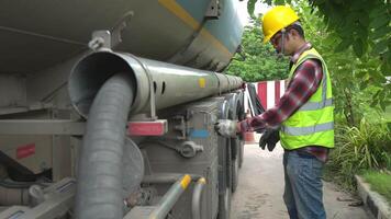 A male Thai worker fills oil with a large pipe into the cap of an oil well tank. video