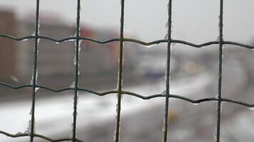A cityscape is visible through a wire fence with a blurred effect on a snowy day video