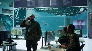 Military specialist handles national safety operations with his crew in a high tech control center, focusing on data protection and surveillance. Soldiers working on intelligence. Camera B. video