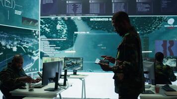 Cybersecurity specialist operates in a high tech military control center, monitoring surveillance footage and gathering intelligence for a new defense mission. Secret service activity. Camera B. video