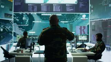 Military specialist in command post uses advanced technology and high tech gear to gather intelligence from satellite imagery and computer surveillance systems to communicate information. Camera B. video