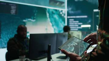Military officer leads cybersecurity operations in a high tech operation room command post, ensuring data protection. Soldiers working with cctv surveillance systems, satellite imagery. Camera B. video