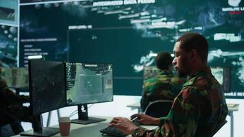 Team of military specialists overseeing surveillance activity by using a cctv footage and radar, pointing at a big screen and world map. High tech control center base of operations. Camera B. video