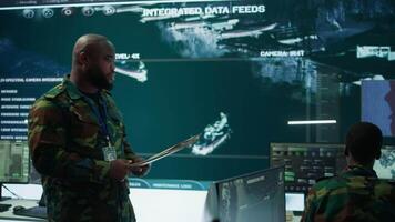 Military staff work in a high tech monitoring room command post, managing cybersecurity operations and surveillance systems. Soldier ensures data protection for national safety. Camera B. video