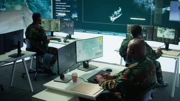 Military personnel in a base of operations using advanced computers and big screen, monitoring satellite systems to enhance security measures and process data. High tech army gear. Camera B. video