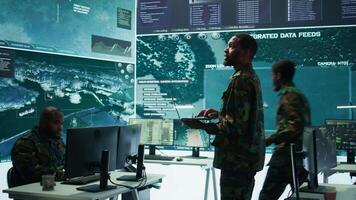 Military officers work in a high tech army control tower base, managing surveillance imagery from cctv satellite. Soldiers handle data protection to ensure national security. Camera B. video