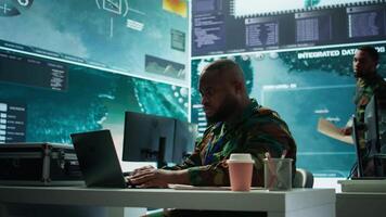 IT analyst in a high tech base of operations handling surveillance activity and ensuring security protocols. Military command post crew collecting real time data to achieve objectives. Camera B. video