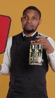 Vertical Catering employee showing a red speech bubble icon in studio, carrying a cruet set with condiments. Waiter with professionalism presenting an empty cardboard sign as an advertisement. Camera B. video