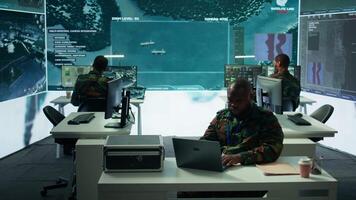 Intelligence agents in modern operations center managing surveillance activity and synchronizing security protocols. Army base staff interpret real time data to protect national interests. Camera B. video