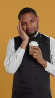 Vertical Tired overworked waiter drinking a coffee cup to relax after long shift, working in catering and service oriented environment. Employee feels fatigued and serving caffeine drink. Camera B. video