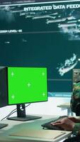 Vertical Military specialist monitors satellite data next to green screen display, working at command post with high tech gear to support army defense operations. Coordinates strategic missions. Camera B. video