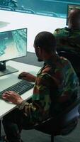 Vertical Military experts in mission control center use modern technology on computer and big screen, analyzing satellite footage. Specialist tracking potential threats for intelligence operations. Camera B. video