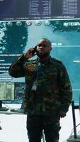 Vertical Military specialist handles national safety operations with his crew in a high tech control center, focusing on data protection and surveillance. Soldiers working on intelligence. Camera B. video