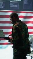 Vertical Professionals in US military uniforms operate computers and big screen, working on surveillance and intelligence to ensure national security from a high tech control center. Camera B. video