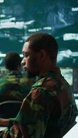 Vertical Team of military specialists overseeing surveillance activity by using a cctv footage and radar, pointing at a big screen and world map. High tech control center base of operations. Camera B. video