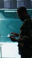 Vertical Cybersecurity specialist operates in a high tech military control center, monitoring surveillance footage and gathering intelligence for a new defense mission. Secret service activity. Camera B. video