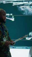 Vertical Military staff work in a high tech monitoring room command post, managing cybersecurity operations and surveillance systems. Soldier ensures data protection for national safety. Camera B. video