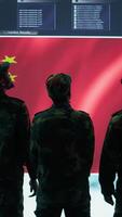 Vertical Cybersecurity specialist in Chinese military command post analyzes data to inflict fear of communism regime. Fake news and propaganda scaring the population, Chinese flag on big screen. Camera B. video