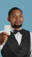 Vertical Classy hotel bellboy in tuxedo giving the room access key card to guest after check in, offering excellent concierge services at holiday resort. Employee working in hospitality industry. Camera A. video
