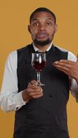 Vertical Restaurant employee bringing a glass of red wine to clients at the table, serving people at a five star diner. Waiter with professionalism focusing on customer satisfaction. Camera B. video