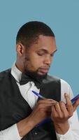 Vertical Receptionist worker writing down notes on clipboard files, ensuring easy check in process for hotel guests against blue background. Bellboy staff providing excellent concierge services. Camera A. video