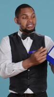 Vertical Hotel concierge showing the check in forms for registration at the five star resort, needs a signature for legal process and formalities. Bellhop receptionist welcoming guests. Camera B. video