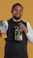 Vertical Skilled restaurant employee waiter presenting electronic payment method, showing the pos terminal with a card in it. Confident catering staff working in a customer focused environment. Camera B. video