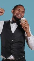 Vertical Hotel concierge staff drinks coffee while he is yawning and feeling tired, trying to get more energy with the caffeine beverage. Doorkeeper employee is exhausted and fatigued. Camera B. video