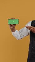 Vertical Waiter with professionalism holding a phone with isolated mockup display, working in dining and eatery industry. Friendly restaurant staff does customer oriented activity at his job. Camera B. video