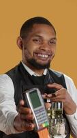 Vertical Skilled restaurant employee waiter presenting electronic payment method, showing the pos terminal with a card in it. Confident catering staff working in a customer focused environment. Camera A. video