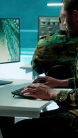 Vertical Military experts in mission control center use modern technology on computer and big screen, analyzing satellite footage. Specialist tracking potential threats for intelligence operations. Camera A. video