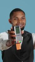 Vertical Hotel porter showing the pos terminal with card to symbolize electronic transaction at front desk. Bellboy with uniform receives payment for the lodging and amenities at the resort. Camera A. video