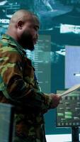 Vertical Military staff work in a high tech monitoring room command post, managing cybersecurity operations and surveillance systems. Soldier ensures data protection for national safety. Camera A. video