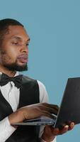 Vertical Bellhop employee making online remote reservations on laptop, browsing the hotel website to check lodging and availability. Doorkeeper staff gives assistance to guests. Camera A. video