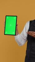 Vertical Waiter showing a tablet with isolated copy space in studio, working in a service oriented environment and catering industry. Friendly restaurant staff serving clients at their tables. Camera B. video