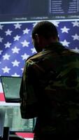 Vertical Professionals in US military uniforms operate computers and big screen, working on surveillance and intelligence to ensure national security from a high tech control center. Camera A. video